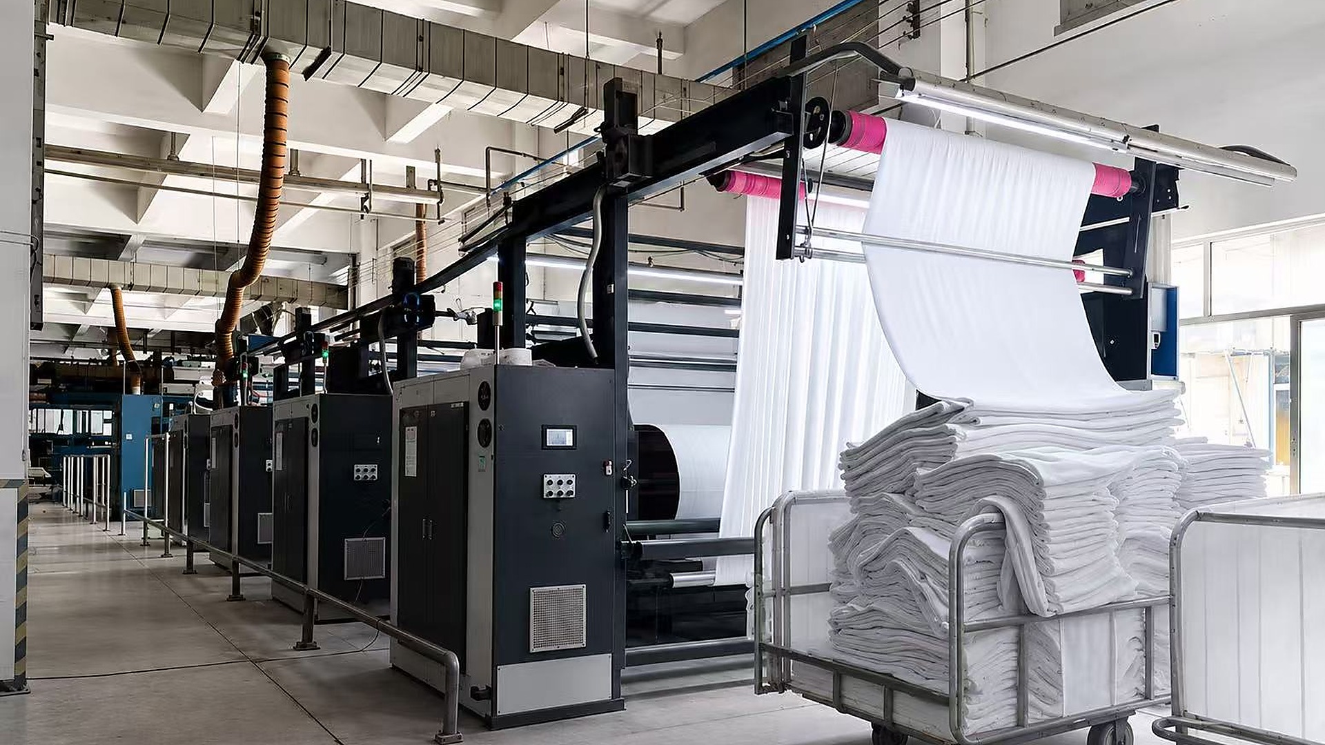 Fabric finishing machines processing white textile rolls